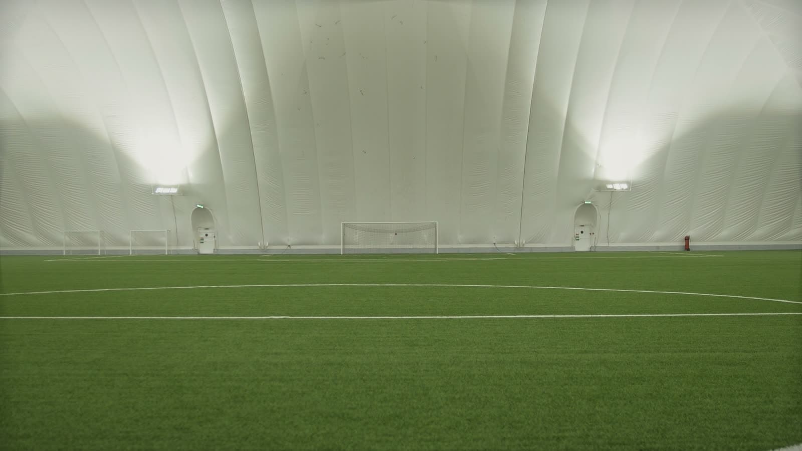 Empty indoor soccer dome with both goals set up and pitch markings visible, no players