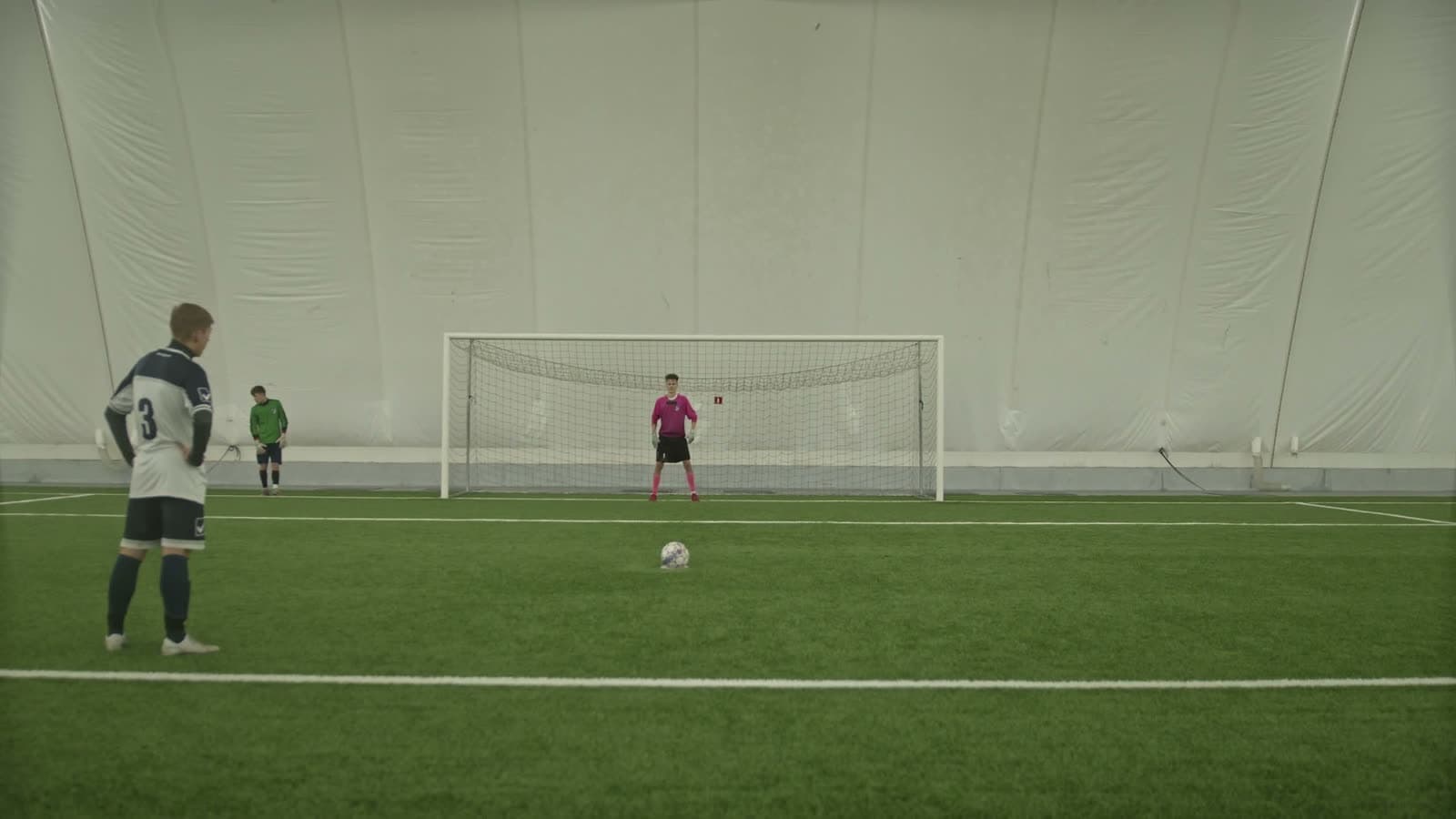Player and goalkeeper facing off in an indoor soccer dome with a penalty shot lined up