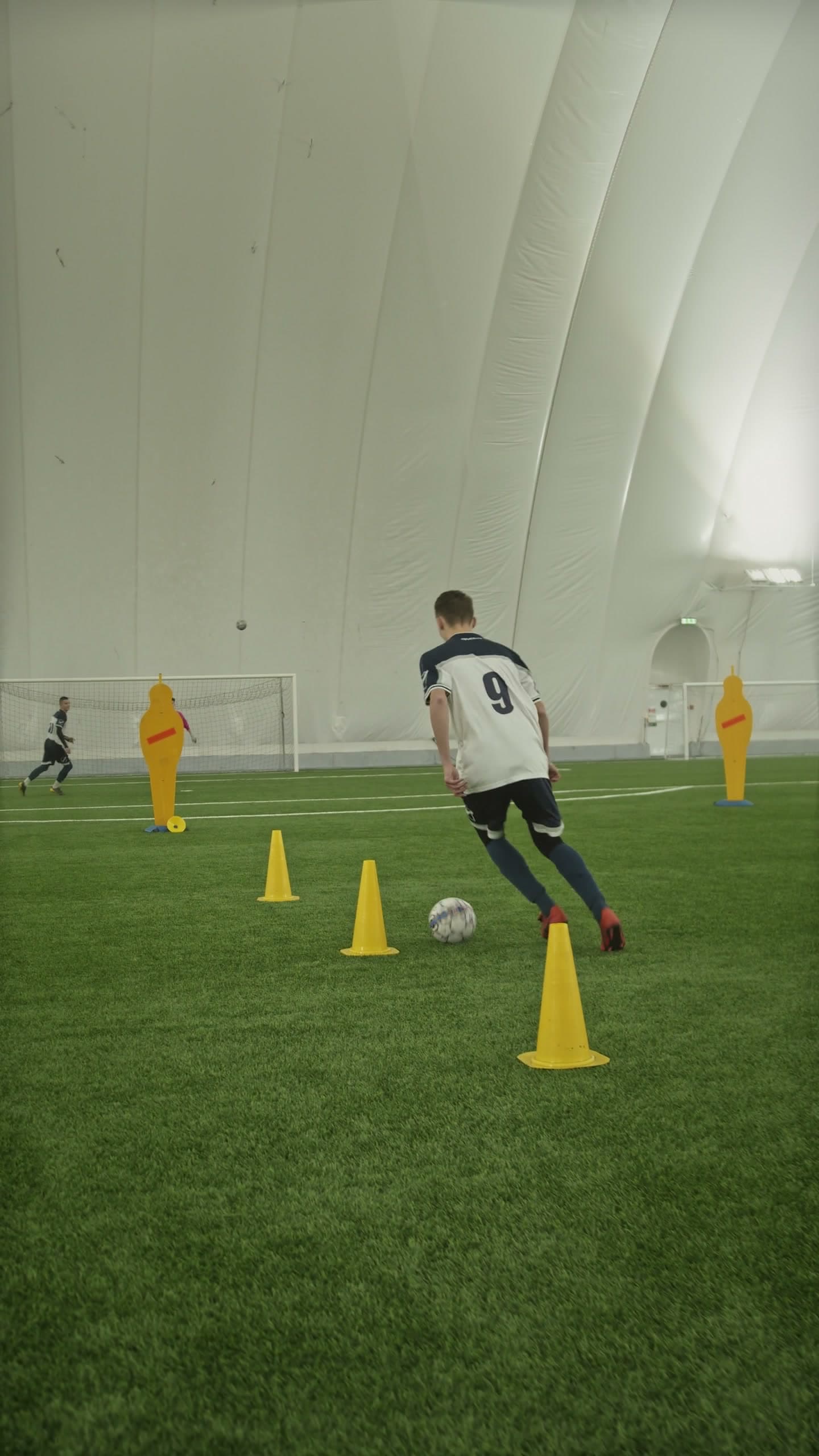 Young player dribbling a soccer ball through a row of training cones during a regular indoor session
