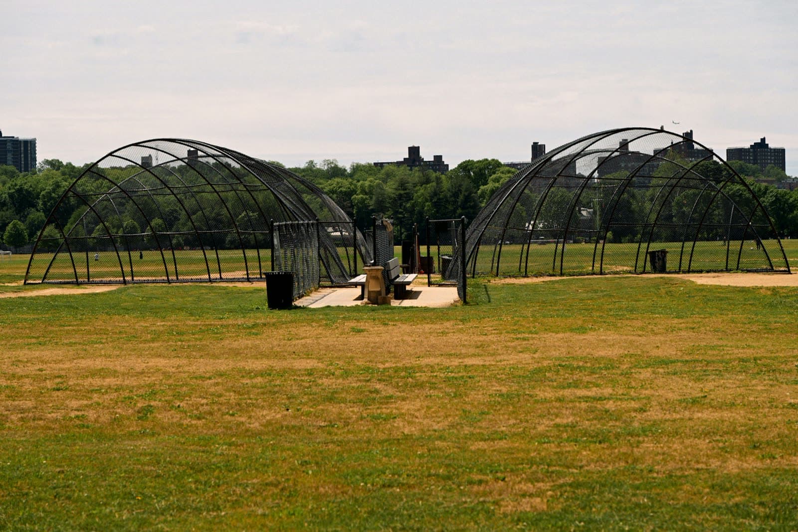 Two arched batting cage structures on an open field