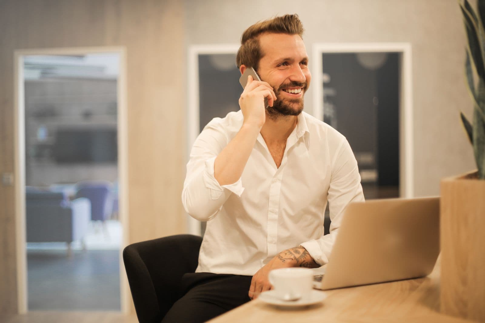 Man sitting at a desk talking on his mobile phone with a laptop open in front of him, trying to complete a booking