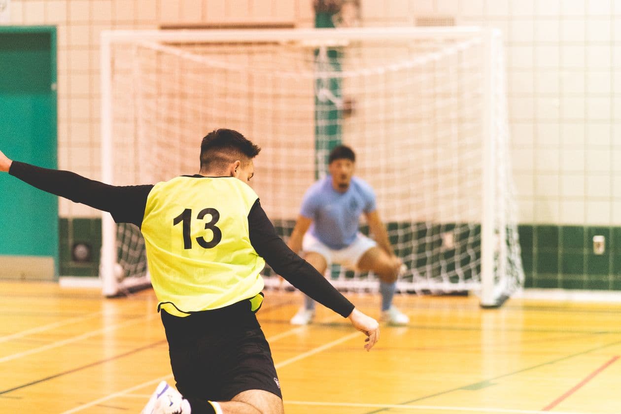Indoor futsal player kicking the ball towards the goal in a competitive indoor match on a hardcourt facility