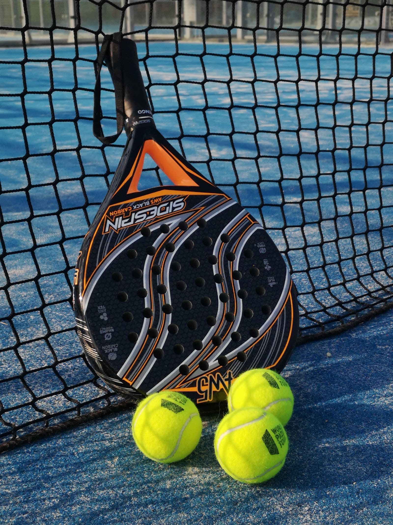 Padel racket and balls resting against the net on court