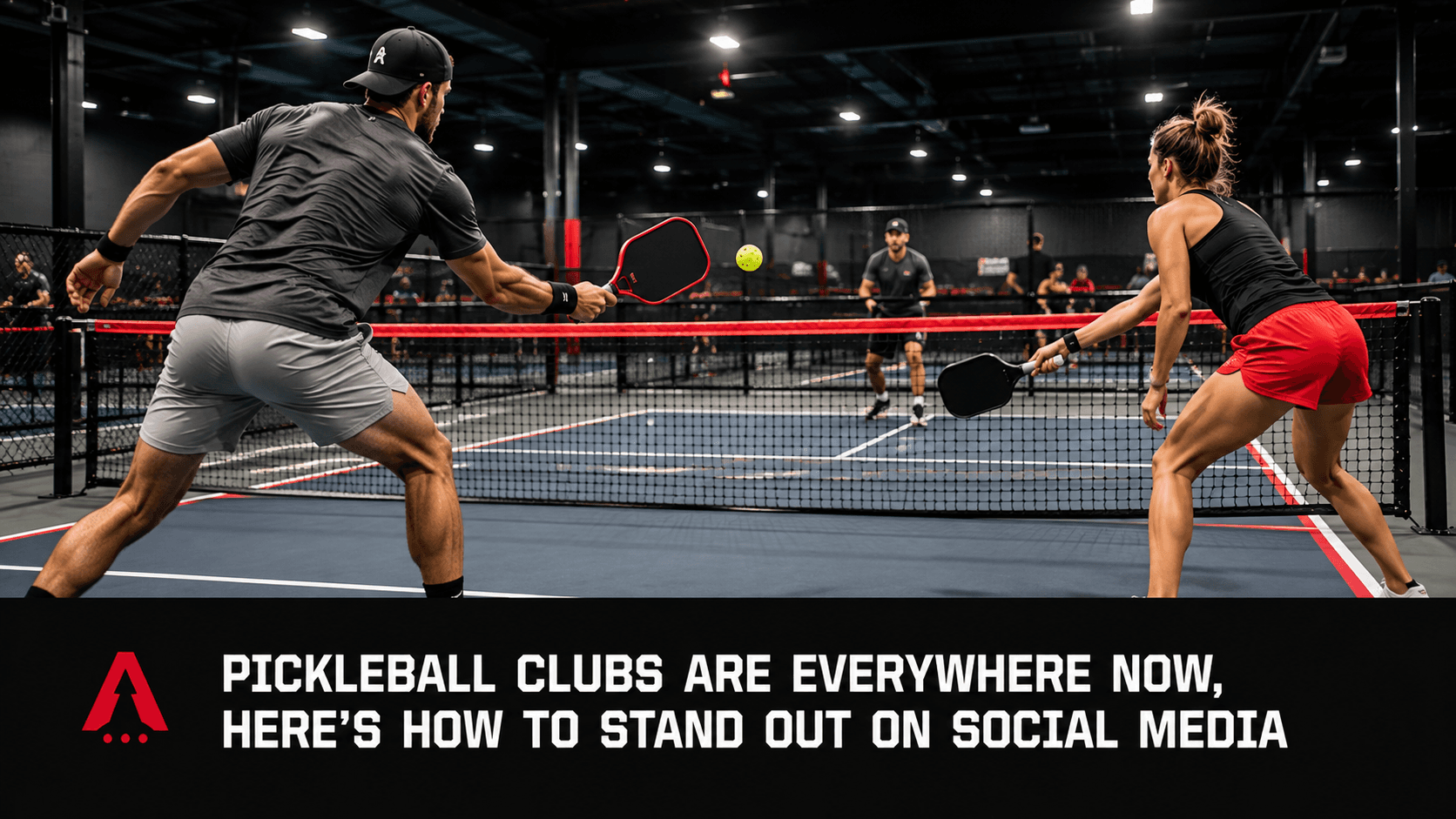 Two pickleball players mid-rally on an indoor court with red and black nets, playing doubles in a modern facility