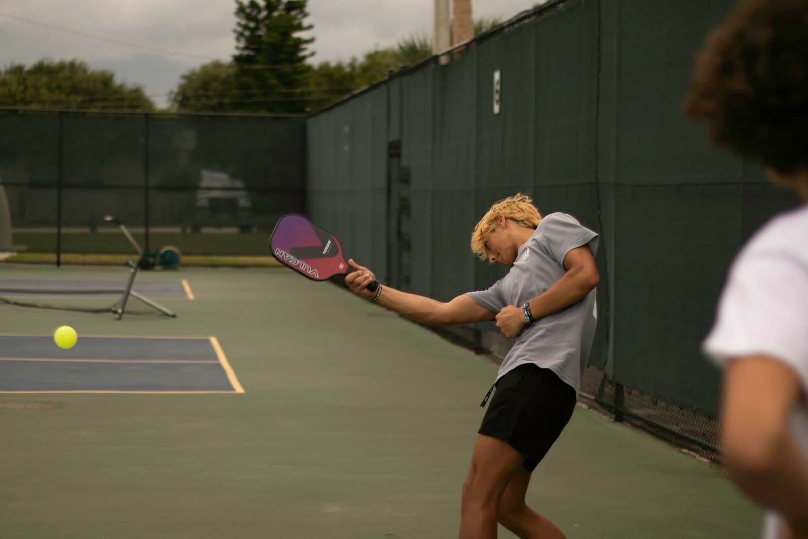 Player swinging a paddle at a yellow pickleball during a match