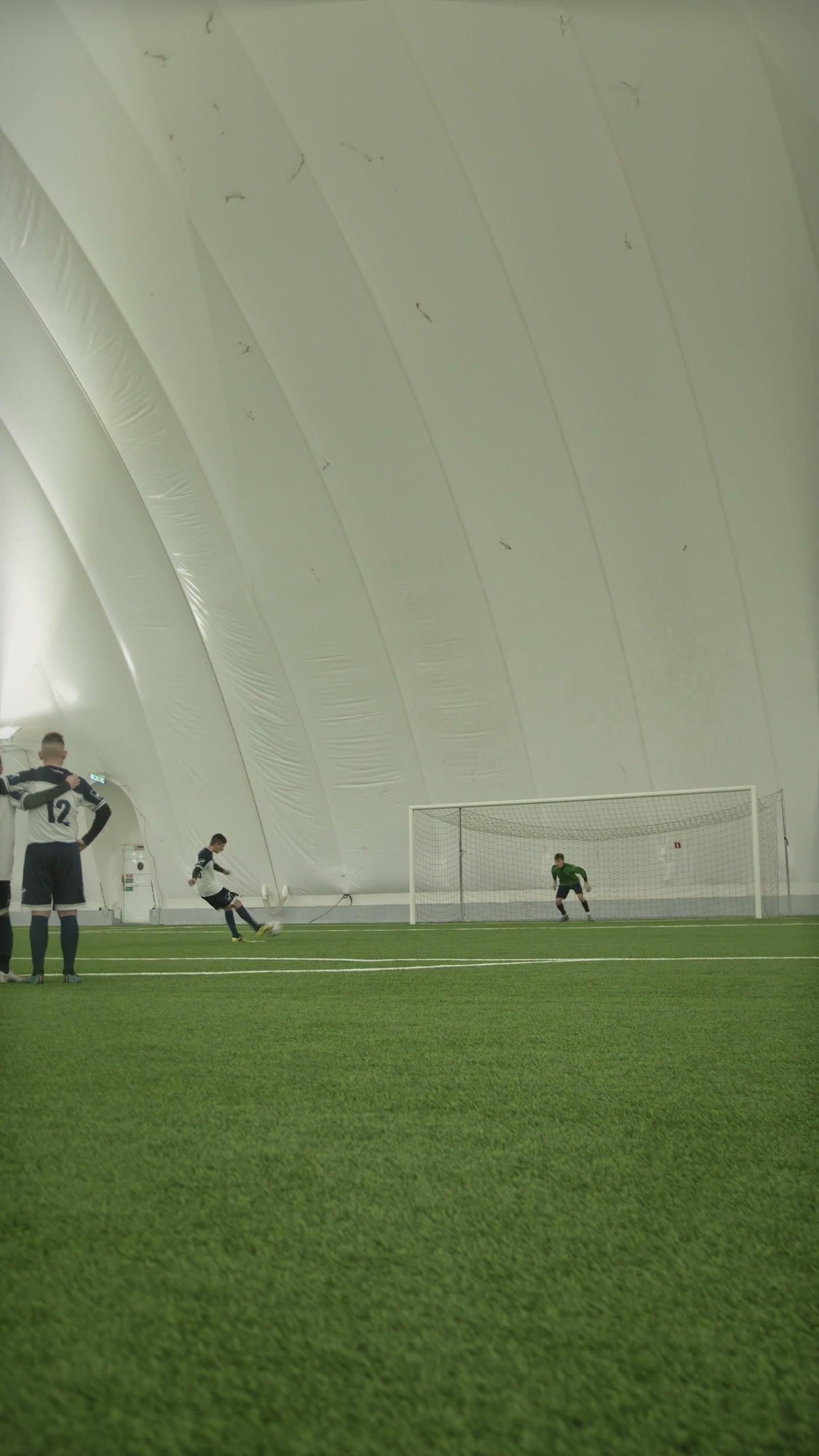 Player striking the ball toward goal as a goalkeeper sets to make a save during an indoor match