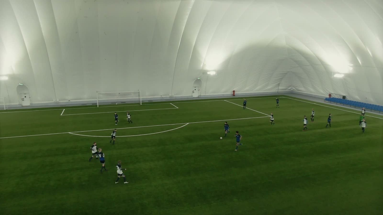 Wide view of a full indoor soccer dome lit up during a match with players spread across the pitch